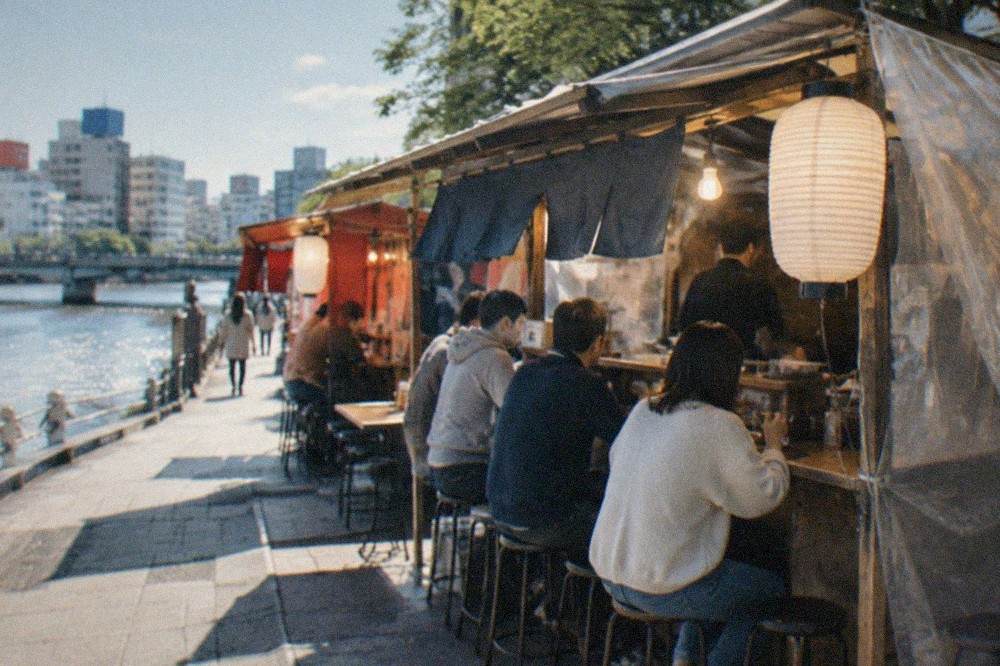 A yatai food stall glowing at night beside a river with customers seated at a small counter