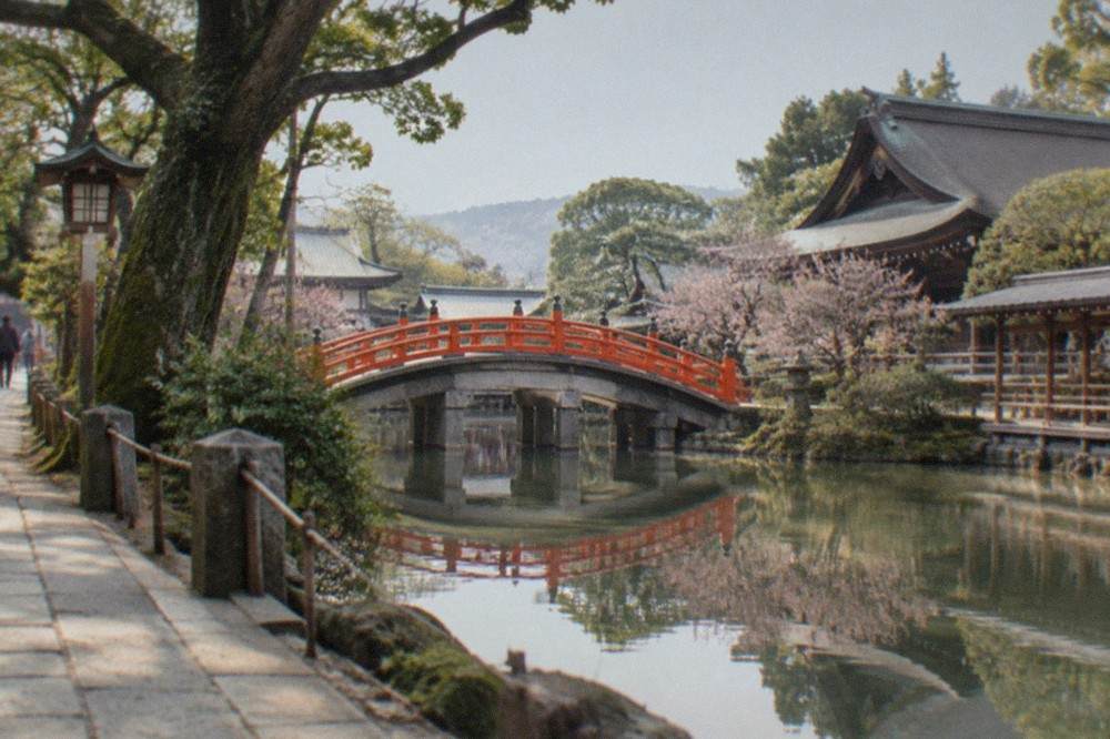 A shrine pond with an arched bridge and trees reflected in still water
