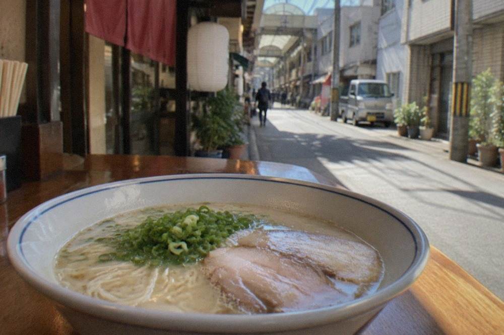 Bowl of milky tonkotsu ramen with thin noodles, chashu pork and green onion on a wooden counter