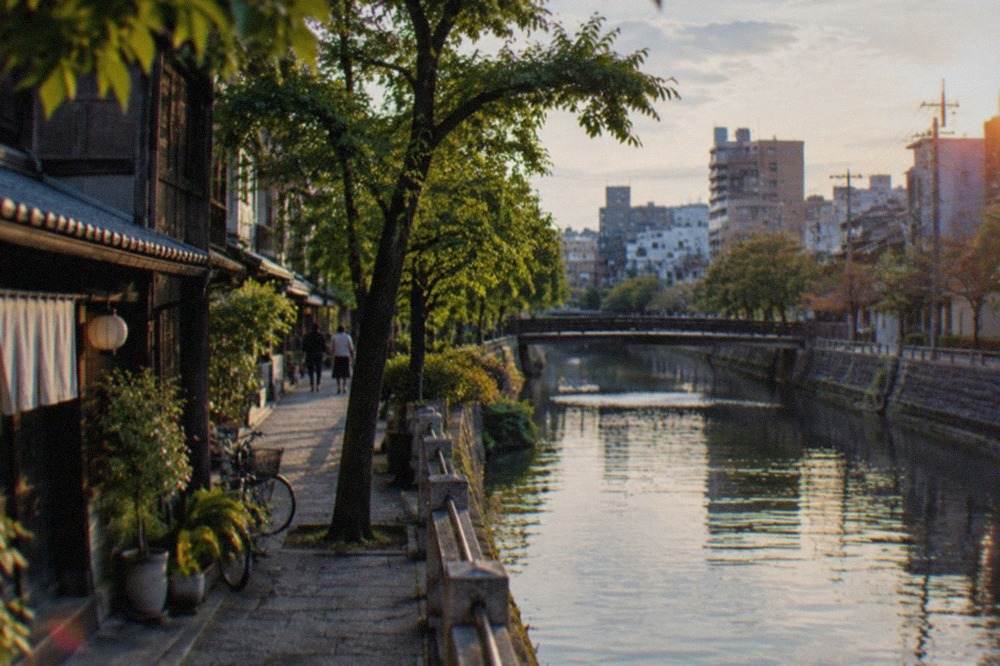 Quiet canal-side stone path lined with trees beside traditional buildings in Fukuoka