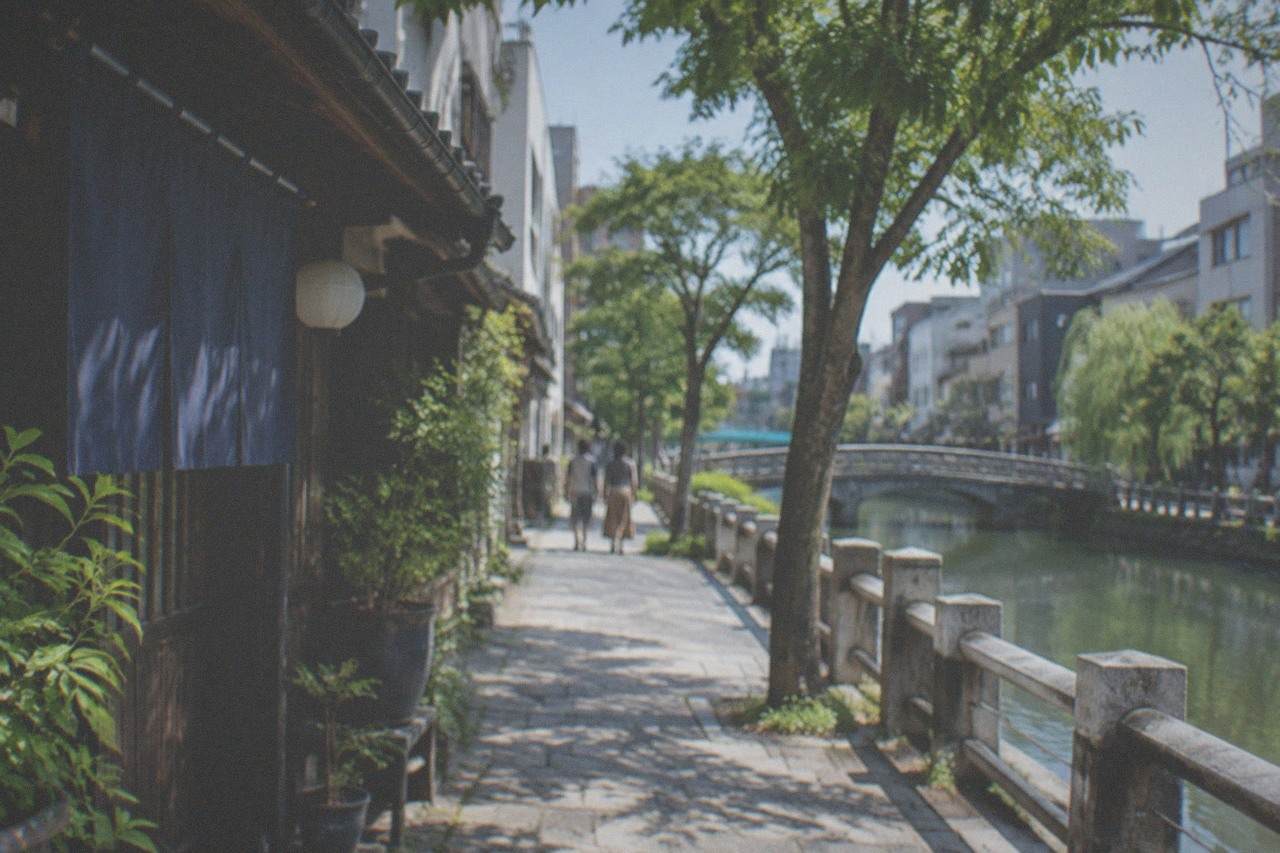 Quiet canal-side stone path lined with trees beside traditional buildings in Fukuoka