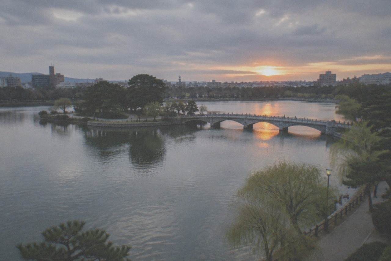 Ohori Park lake at sunset with the city skyline and a stone bridge across calm water