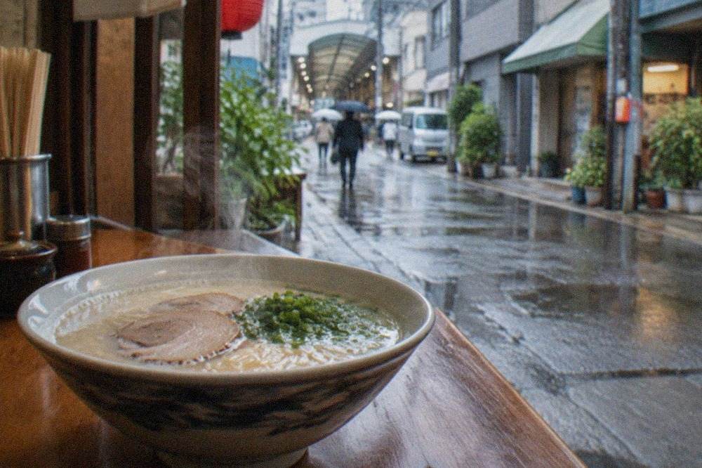A steaming bowl of tonkotsu ramen with thin noodles, sliced pork and green onion on a wooden counter