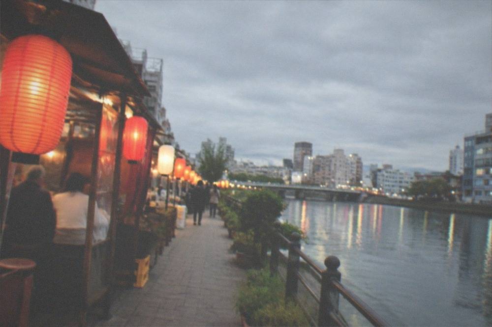 Lanterns glowing over food stalls along a riverside walk in the evening