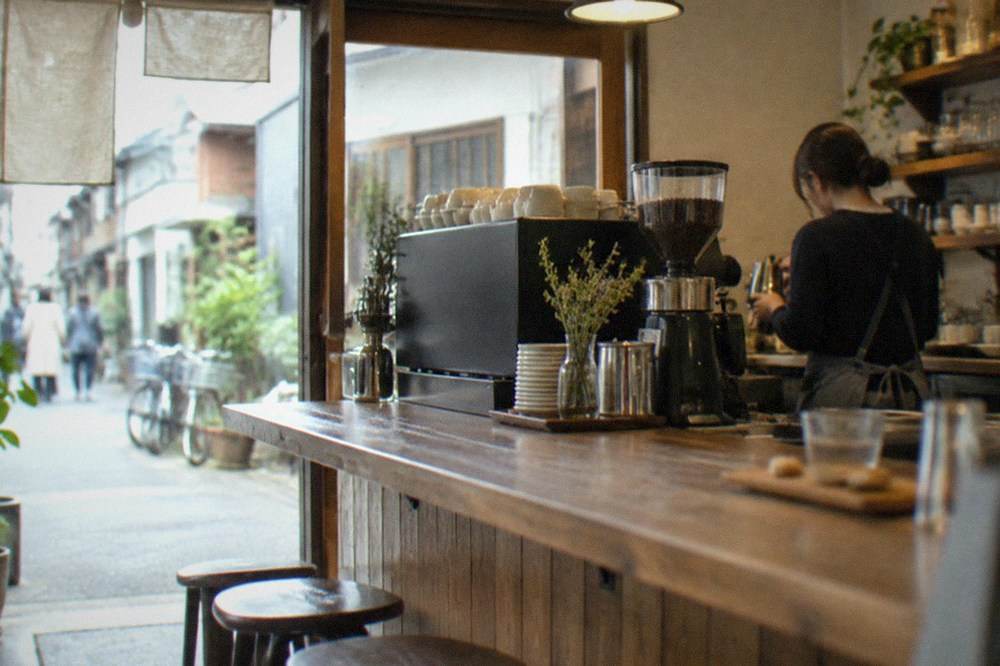 A small independent coffee shop interior in Imaizumi with a wooden counter and a barista at work