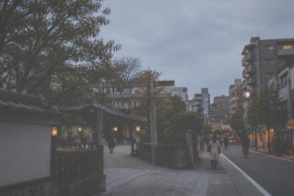 A residential city street at dusk with apartment buildings and lit shopfronts