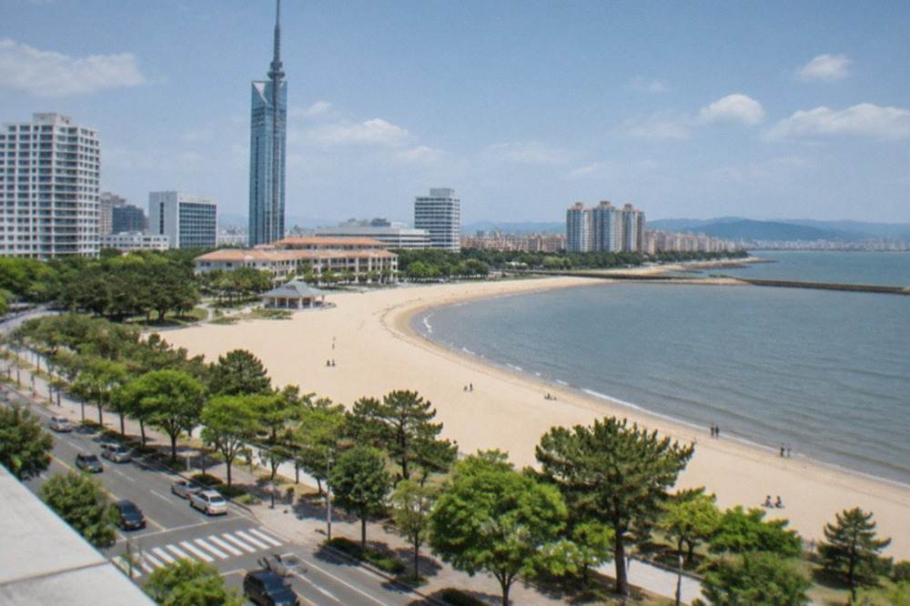 A wide sandy beach with a tall seaside tower and low resort buildings behind it under a bright sky