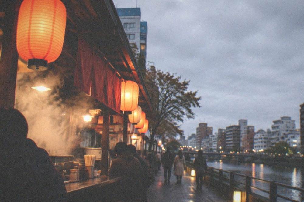 Steam rising from a food stall counter with lanterns glowing at dusk