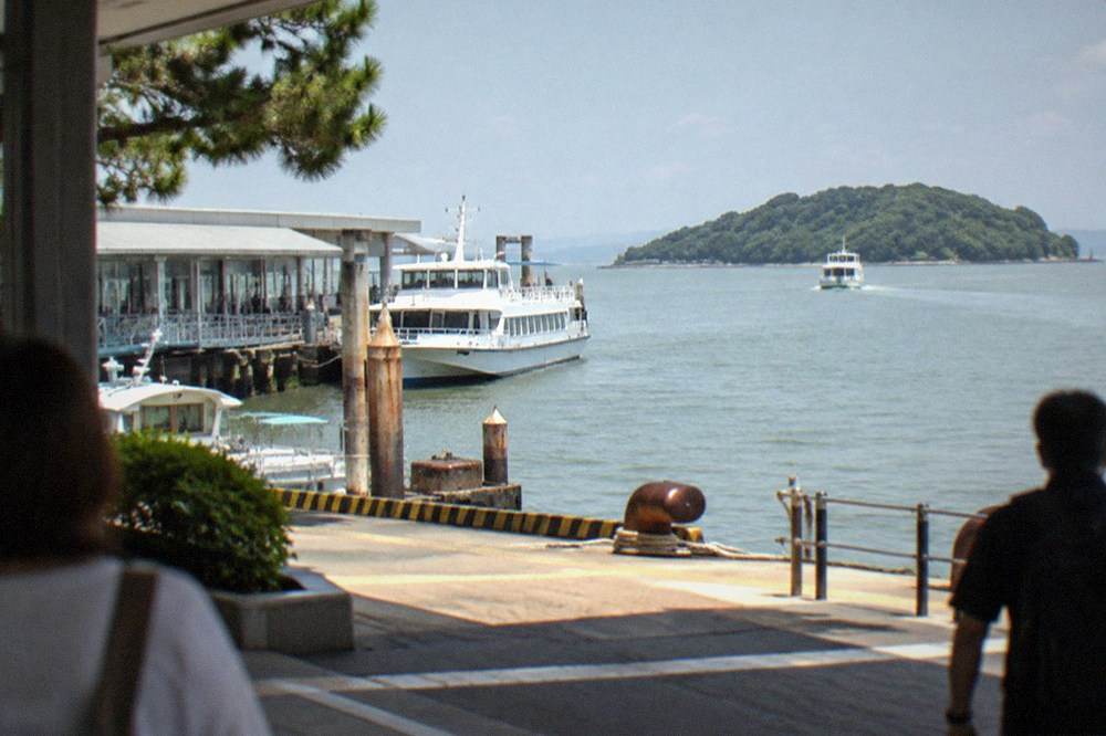 Small passenger ferry moving across calm bay water toward a green island