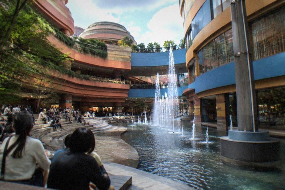 A wide plaza with tiered stone steps where crowds sit watching a fountain