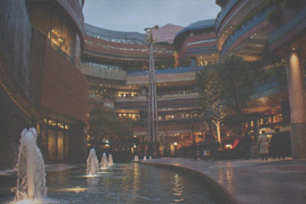 An evening plaza lit with warm lighting beside a lit-up building facade