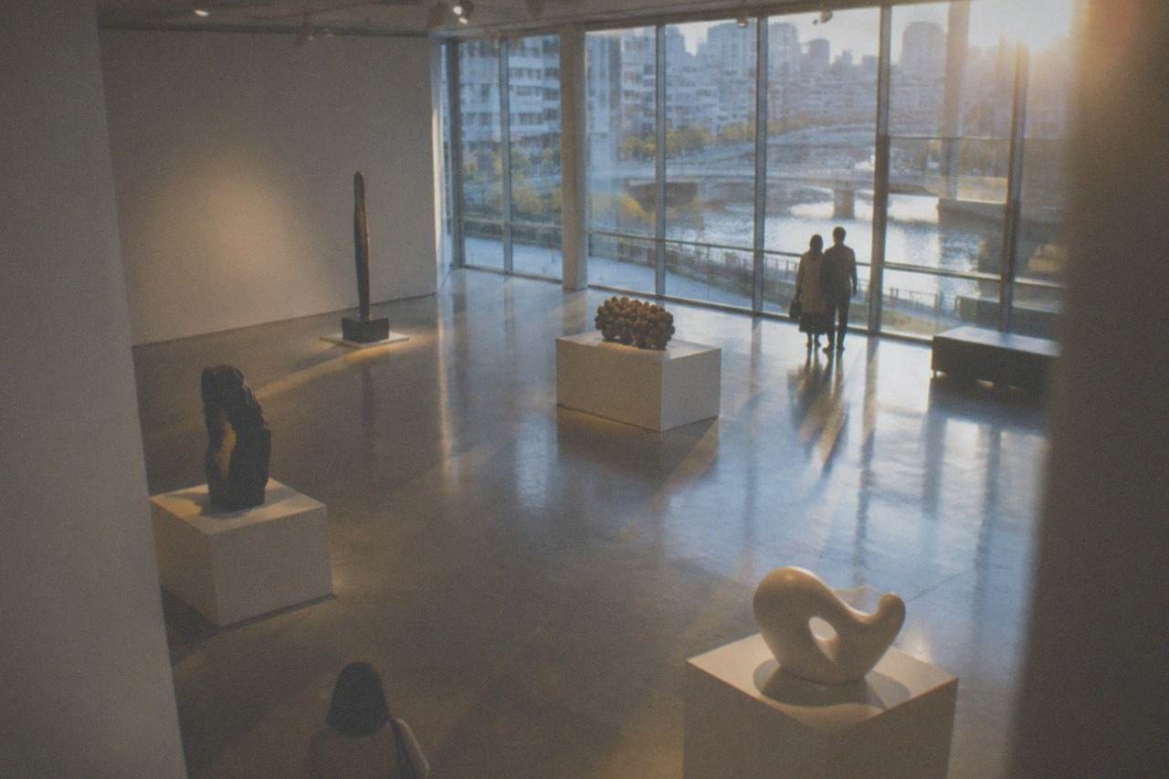 Museum gallery interior with contemporary sculptures displayed on pedestals under soft lighting