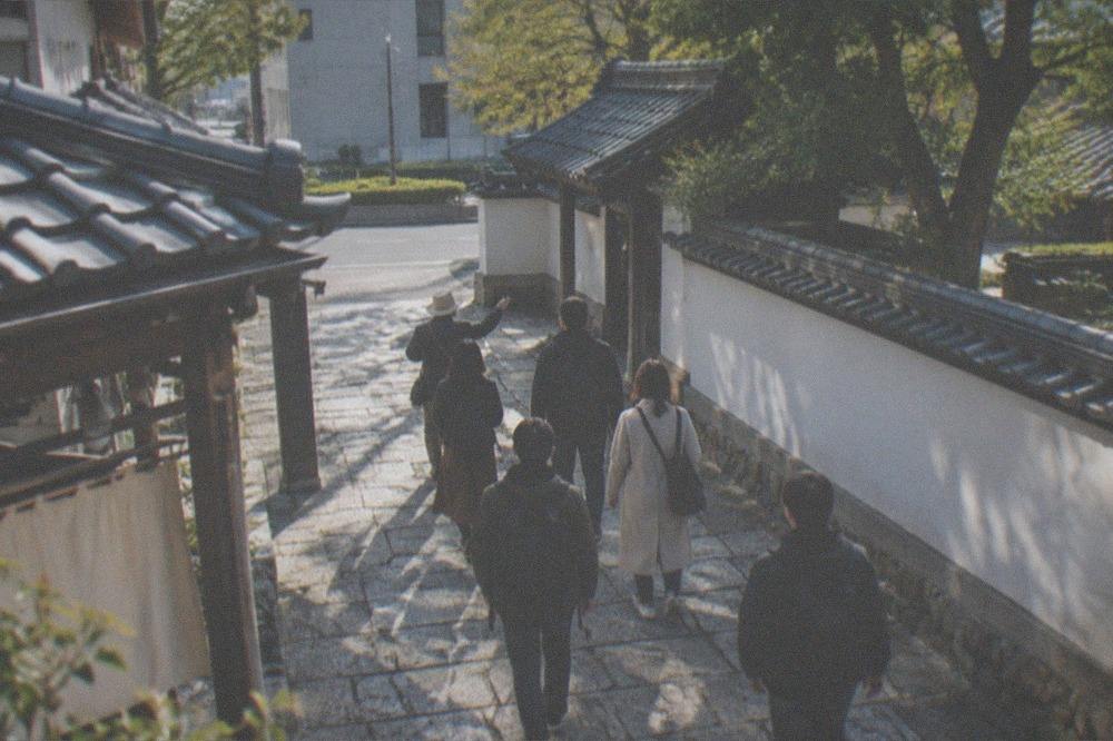 A guide and small group of visitors walking a stone-paved lane between traditional buildings.