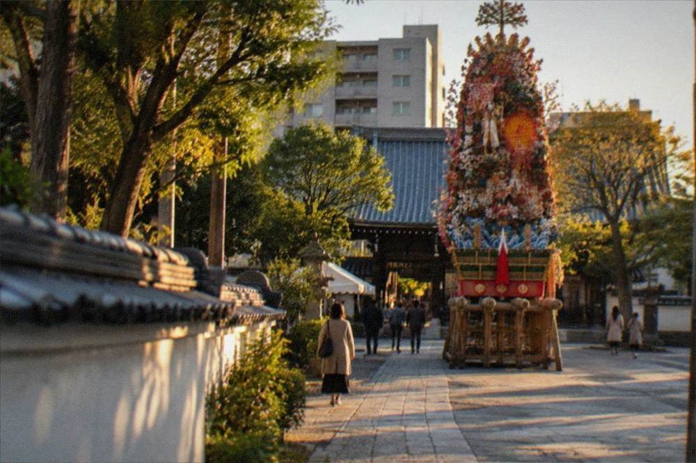 A shrine courtyard with a tall decorated festival float on display under a clear sky.