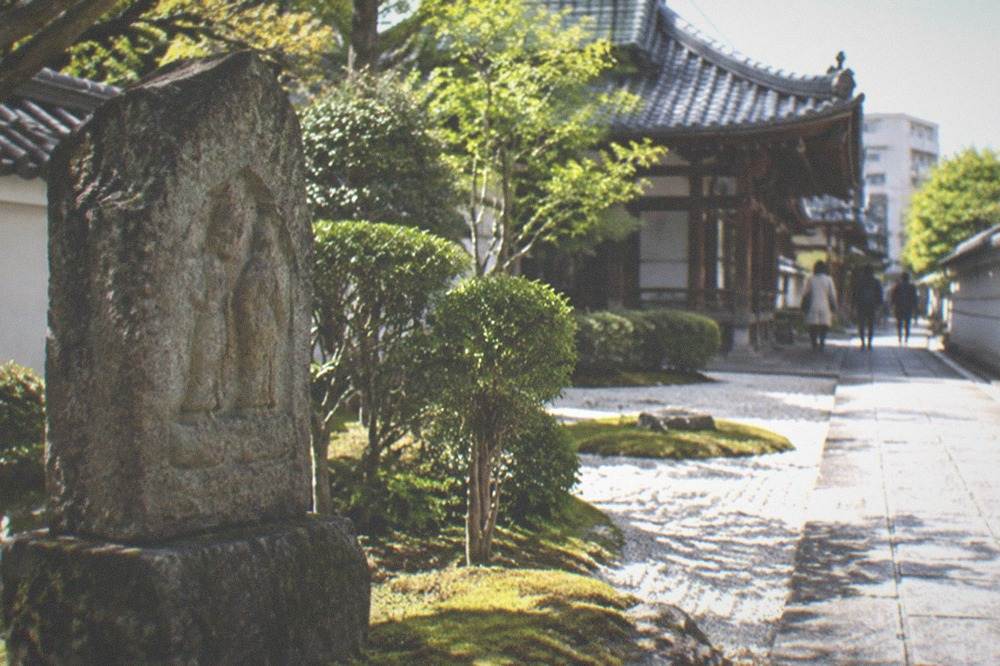 Carved stone monument standing in moss at a temple courtyard edge