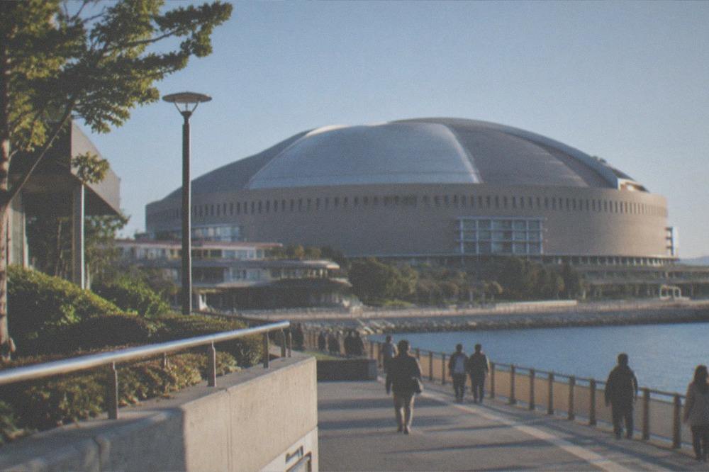 A waterfront promenade under a clear sky with a stadium roof in the distance