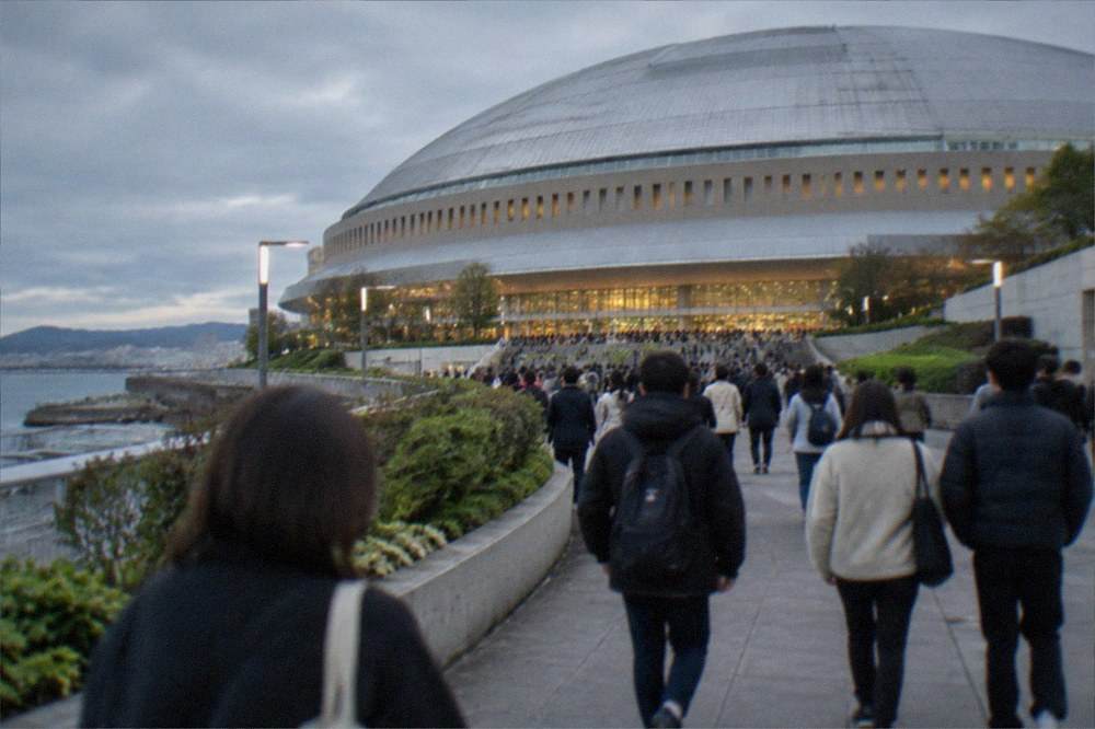 A crowd walking toward a domed stadium entrance under evening lights