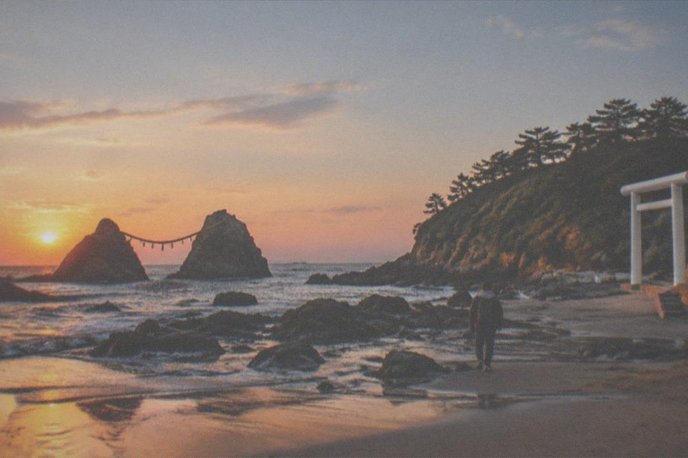 Wet sand at low tide reflecting an orange sky, with dark rocks standing in shallow water