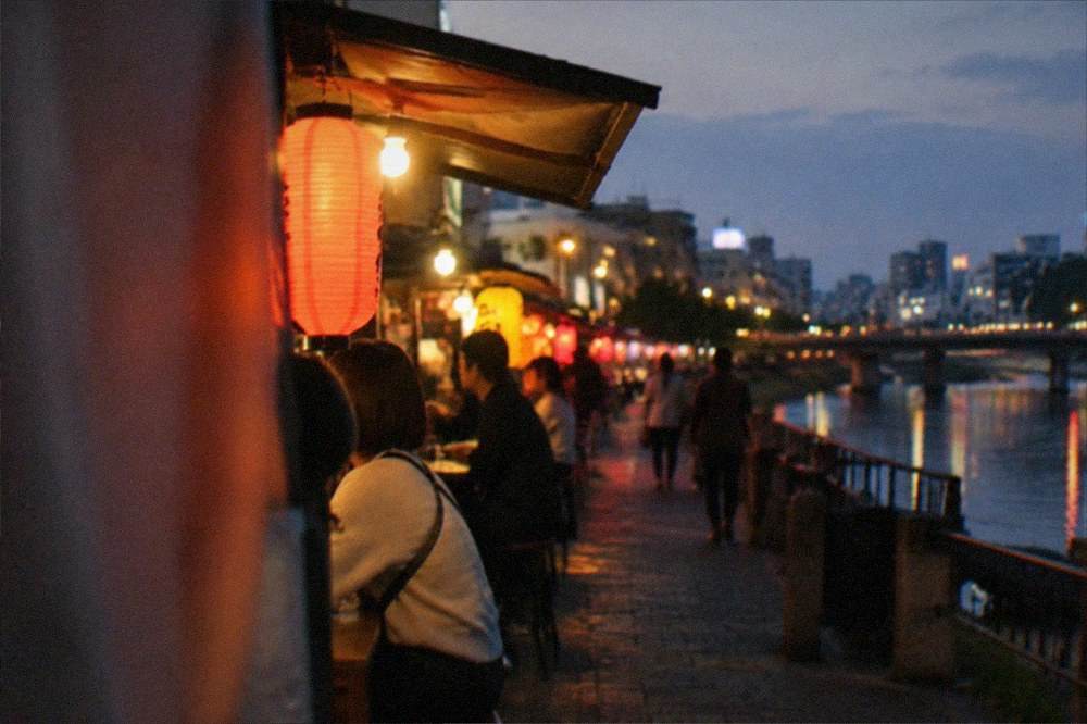 A row of lantern-lit food stalls along a river at night