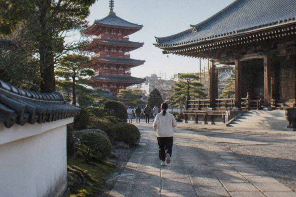 A large wooden temple hall with a wide roof and stone paving under a clear sky