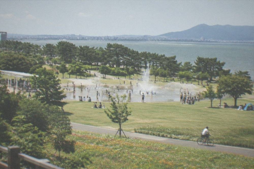 A shallow water play area with sprinklers and fountains on a hot day, surrounded by lawns