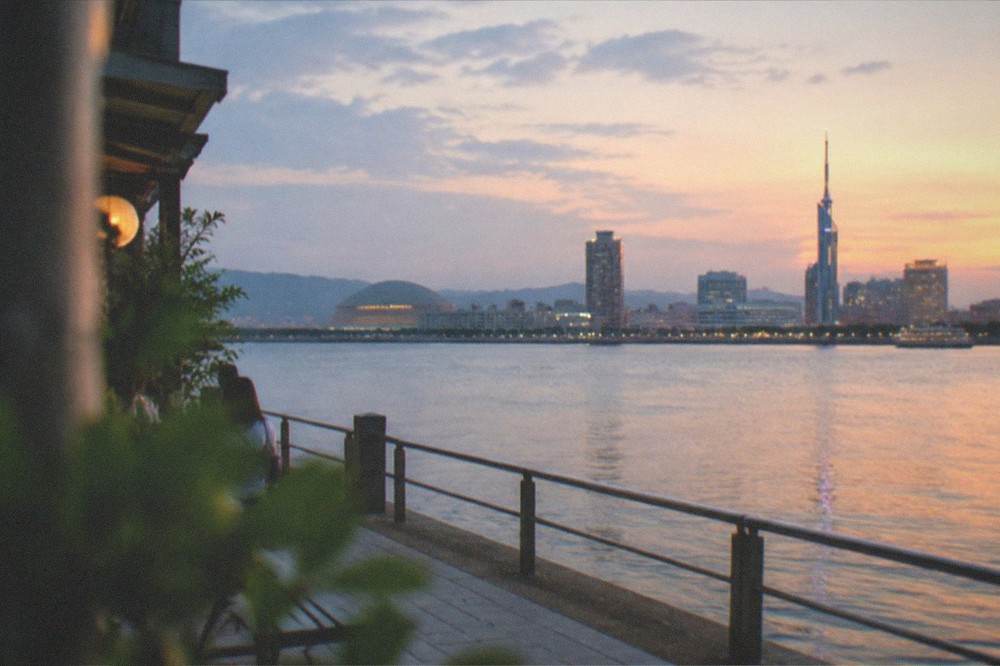 A wide view across Hakata Bay at dusk, with the city skyline lit and calm water in the foreground