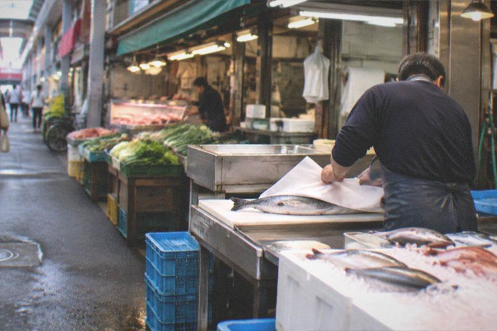 Vendor wrapping a fish purchase in paper at a small market counter