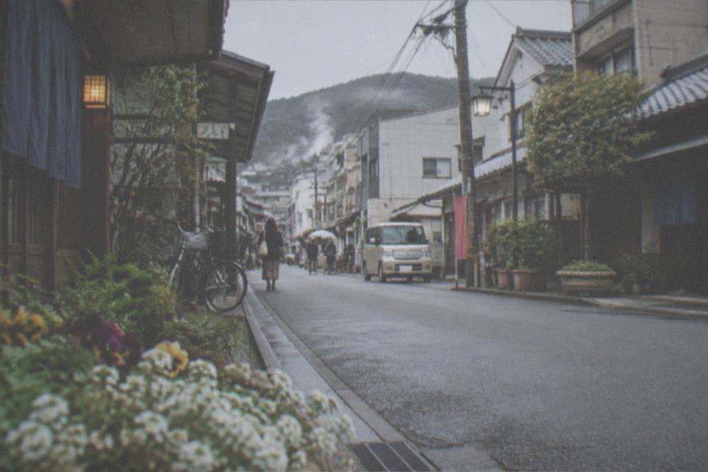 Small onsen town street under a mountain with steam rising between tiled roofs