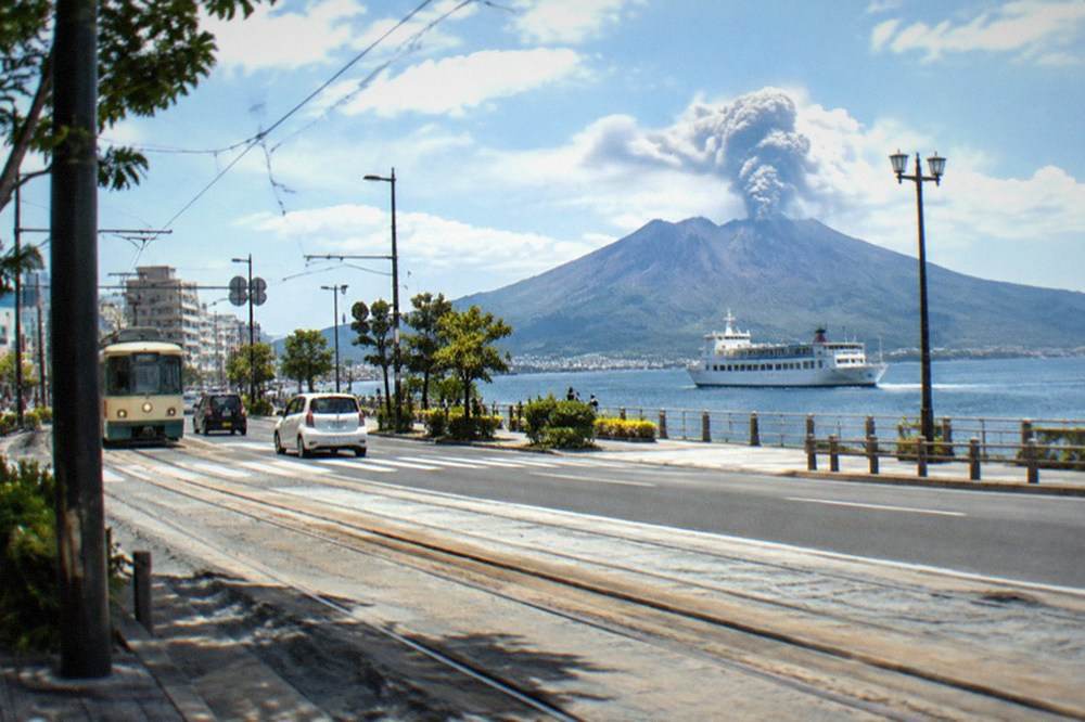 A ferry crossing a calm bay toward a volcanic island under scattered clouds