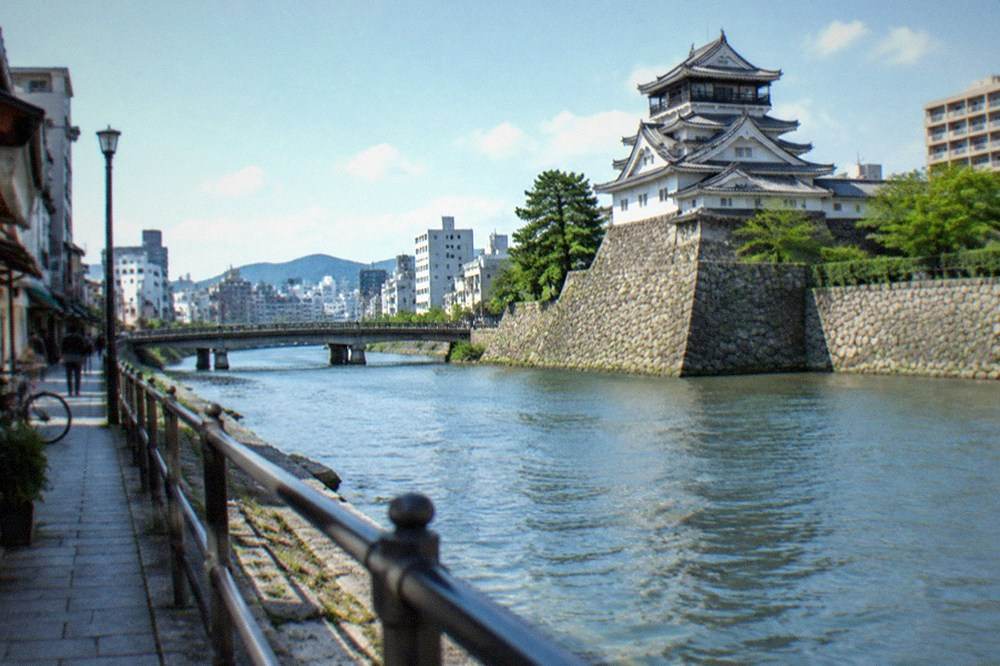 Stone banks of the Murasaki River running between low buildings in Kokura