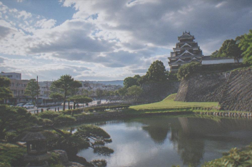 A Japanese stroll garden with a pond, clipped pines and a stone lantern along the water's edge