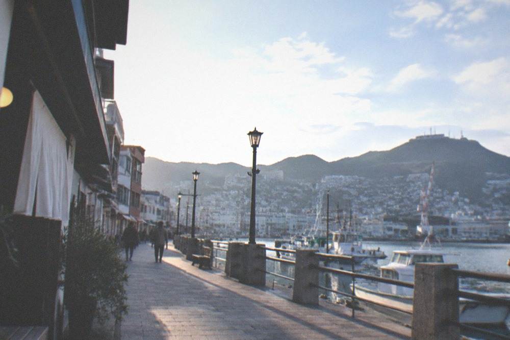 Waterfront promenade with moored boats and hills in the background