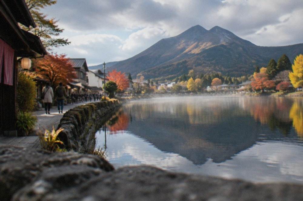 A calm lake reflecting a mountain and autumn trees beside a small onsen town street