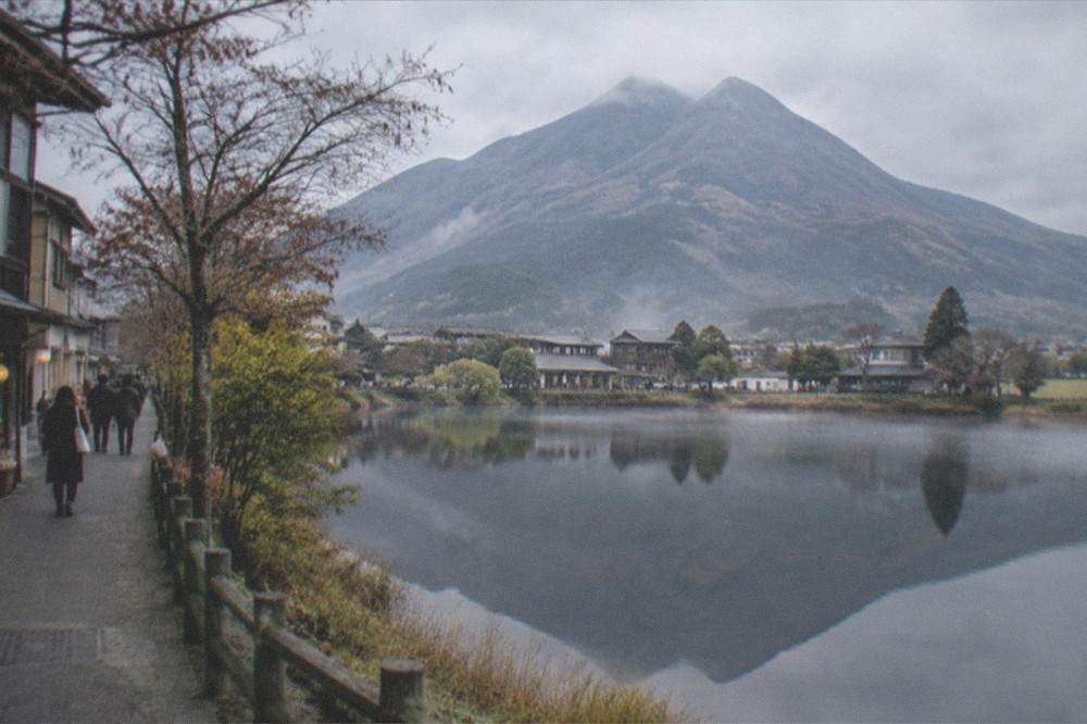 A mountain reflected in a still lake beside a path with scattered trees