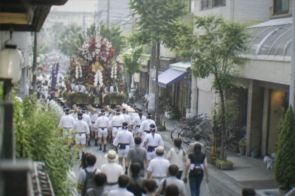 Men in traditional dress carrying a large decorated festival float through a crowded street