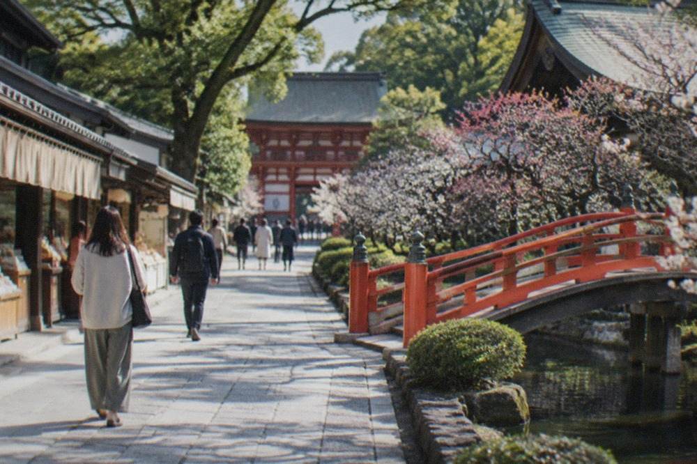 Stone approach path lined with shops leading toward a vermilion shrine gate among trees