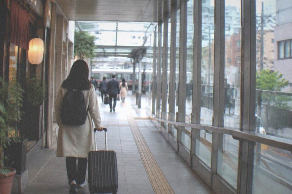A traveler walking through a glass-covered walkway with luggage toward a city-bound train