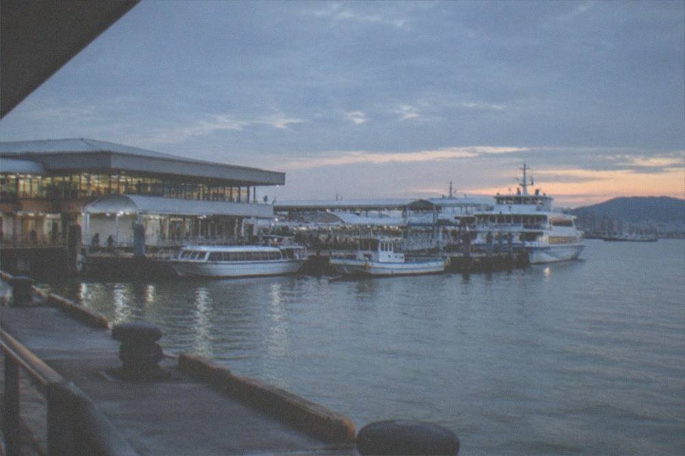 A ferry terminal building beside calm harbour water with moored boats in the foreground