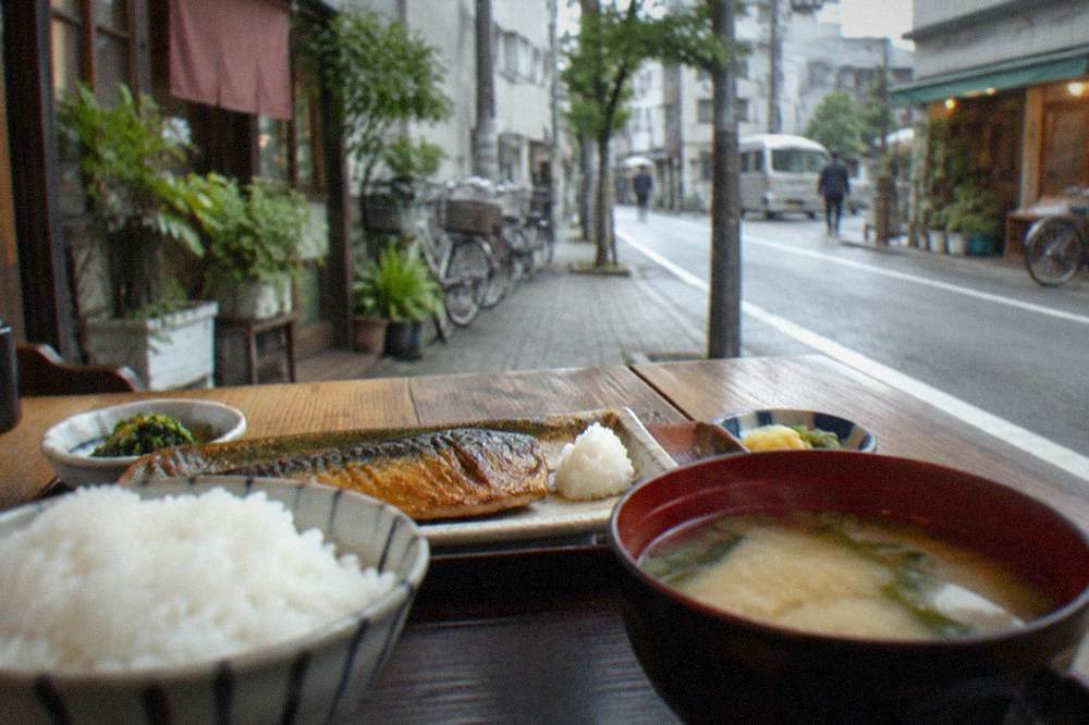 A traditional Japanese breakfast tray with rice, miso soup and grilled fish on a wooden table