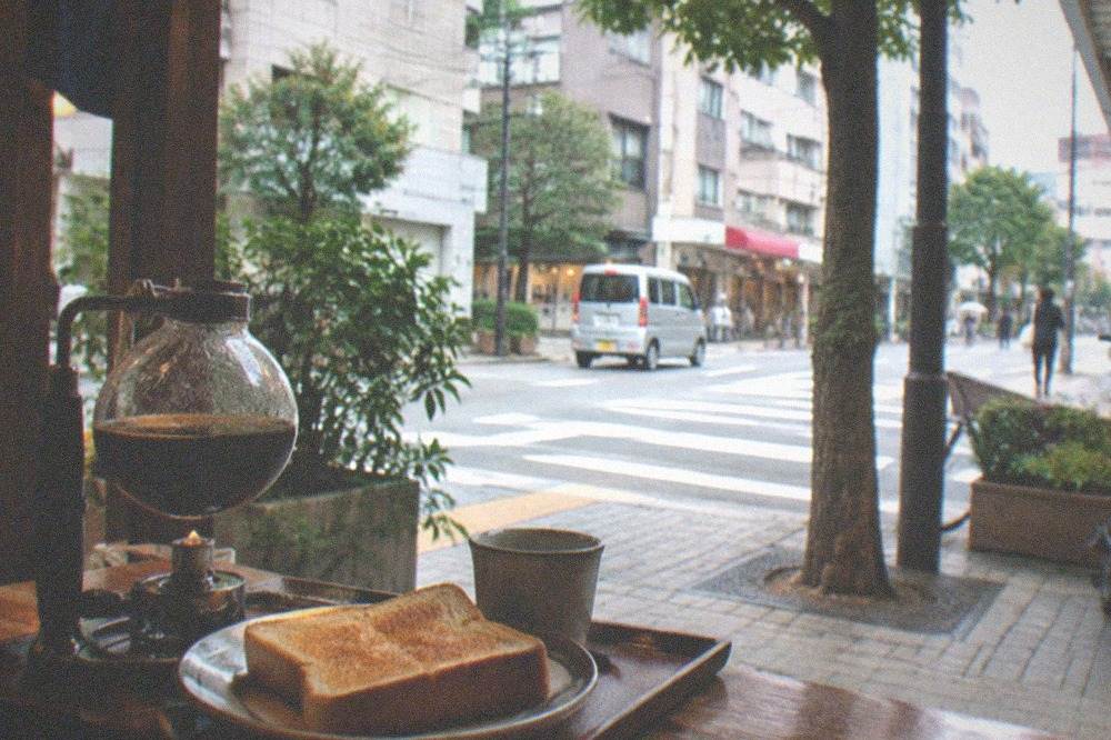 A cup of siphon coffee in a glass flask beside a plate of thick toast on a tray