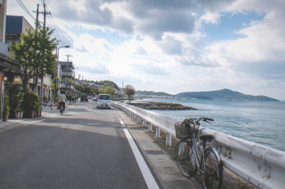 A coastal road with a bicycle leaning against a guardrail and the sea of Itoshima beyond