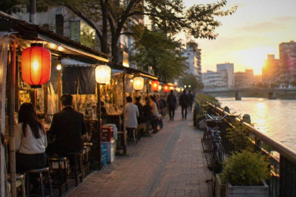 Row of illuminated food stalls along a river at night