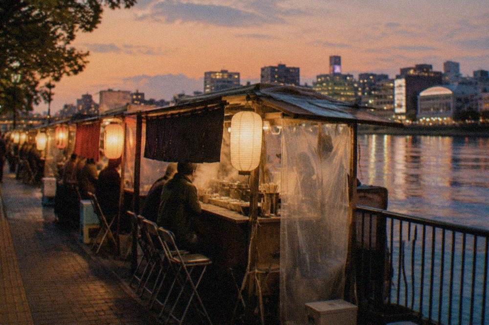 Food stalls with glowing lanterns along a riverside street at night
