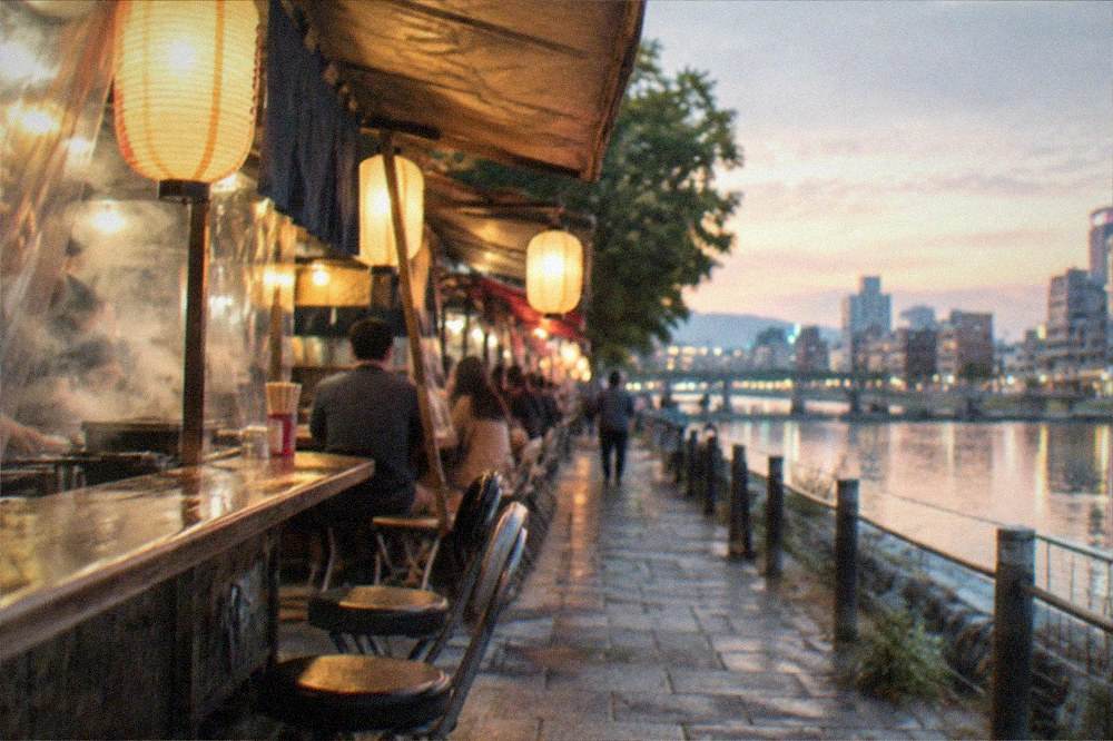 Small alley of evening food stalls lit by lanterns beside a canal
