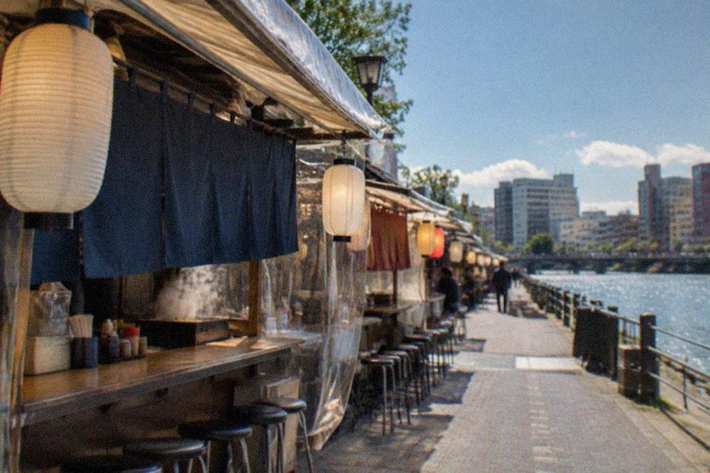 A row of illuminated yatai food stalls along a riverbank at night
