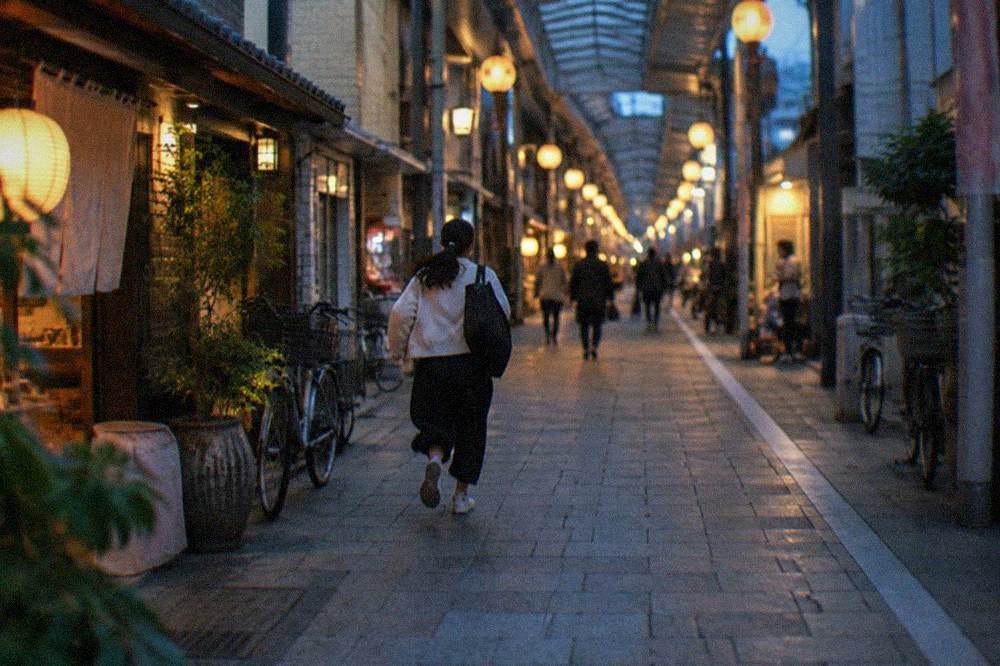 A covered shopping arcade with lantern-lit shopfronts receding into the evening distance