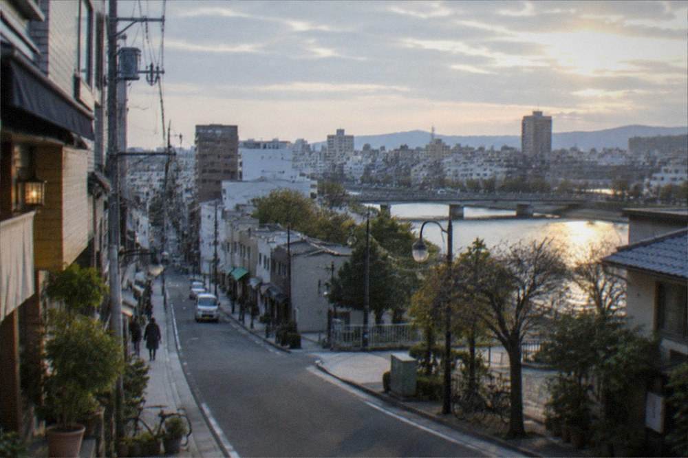 A city skyline at dusk with a river reflecting neon signs and a bay beyond