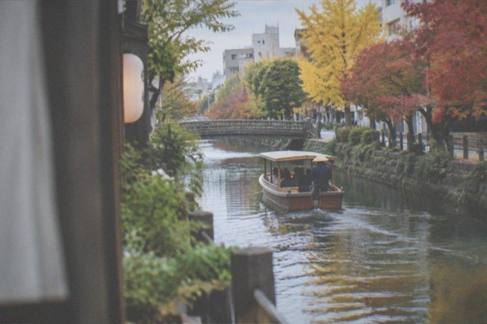 A canal boat gliding between autumn trees in a small Japanese canal town
