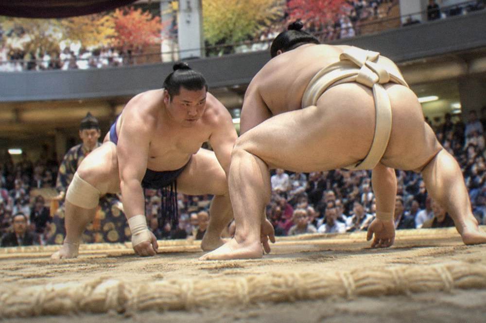 Sumo wrestlers competing on a clay dohyo ring before a full arena