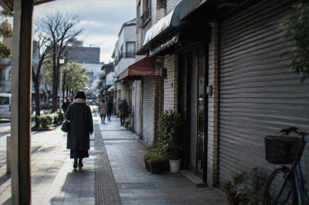 A city street on a cold morning with a person in a long coat walking past closed shop fronts
